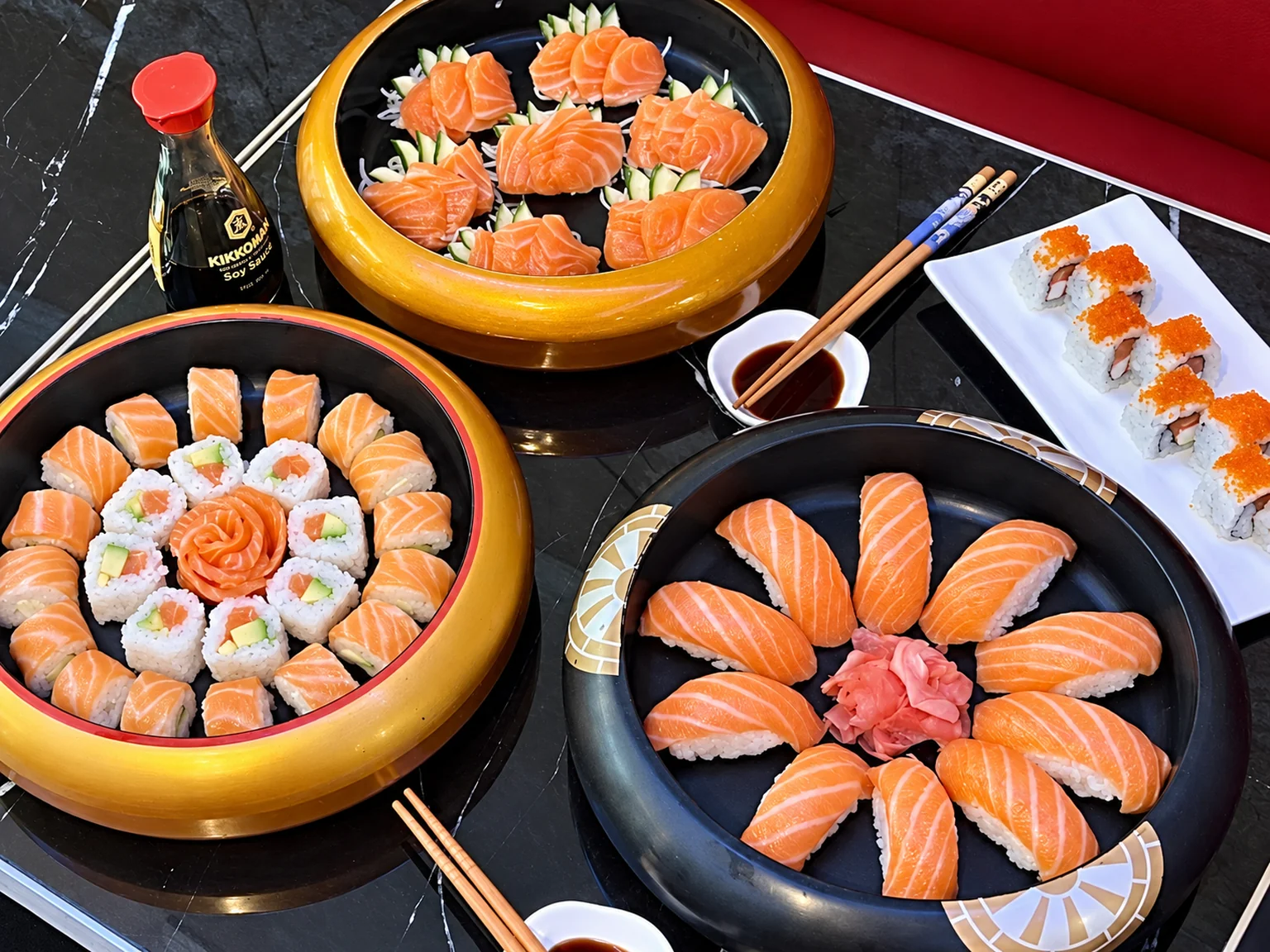 Salmon sushi and sashimi in gold and black bowls on a black marble table.