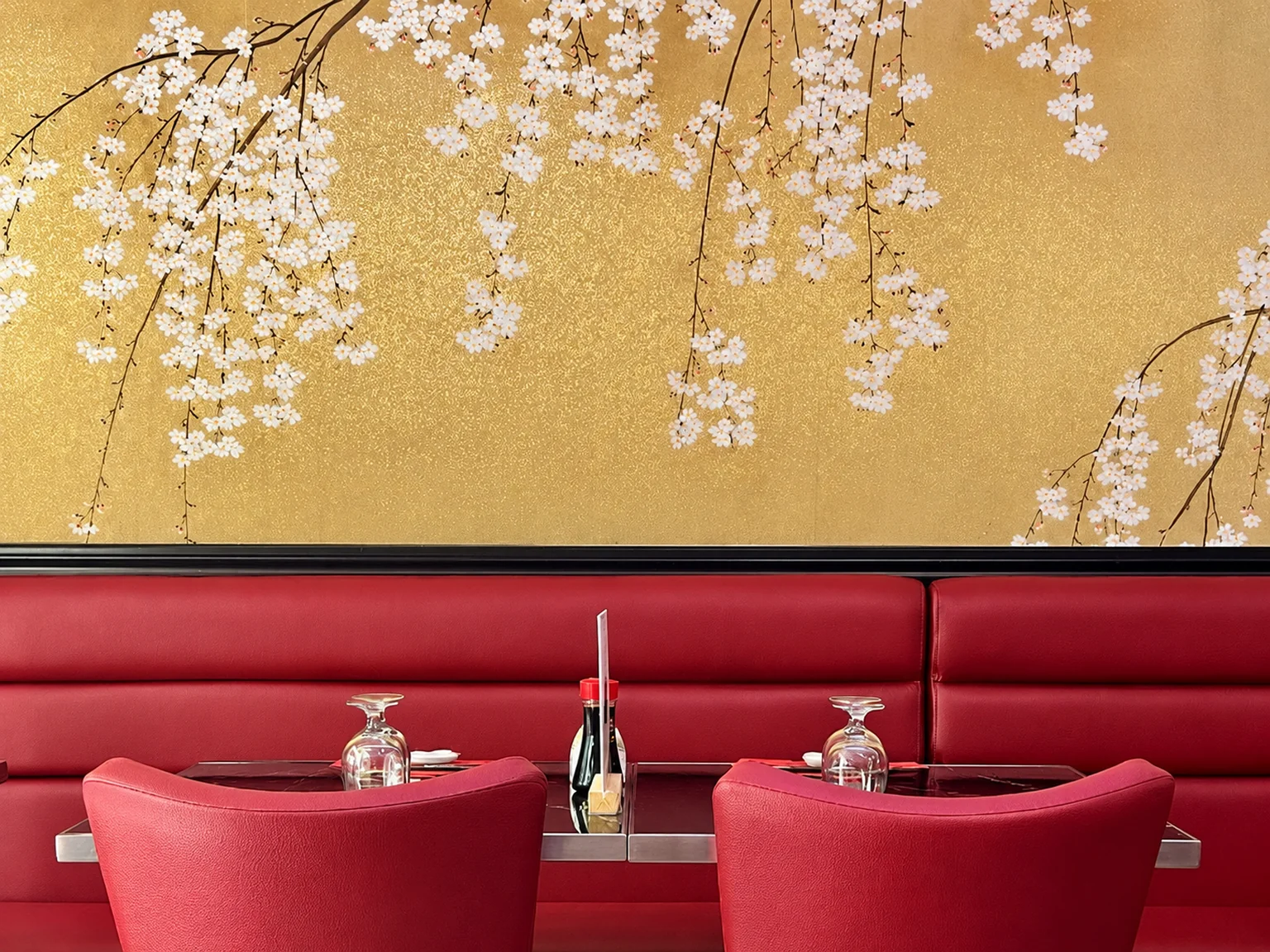 Red banquette and two red chairs in front of a cherry blossom mural on a gold background.