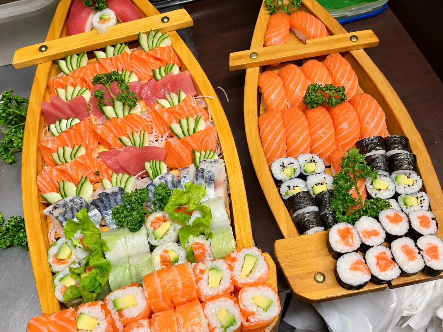 Two wooden boats filled with sashimi, sushi and maki.