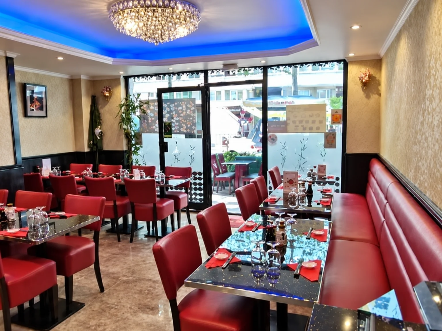 The dining room with red chairs and banquette, blue-lit ceiling and crystal chandelier.